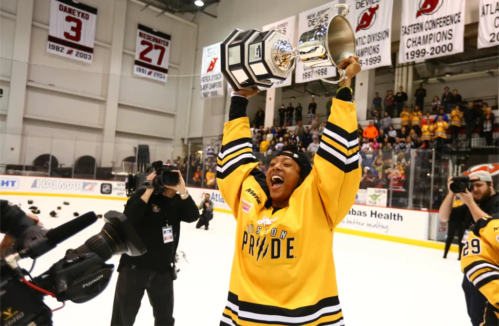 Blake Bolden in a Boston Pride jersey lifting a championship cup over her head