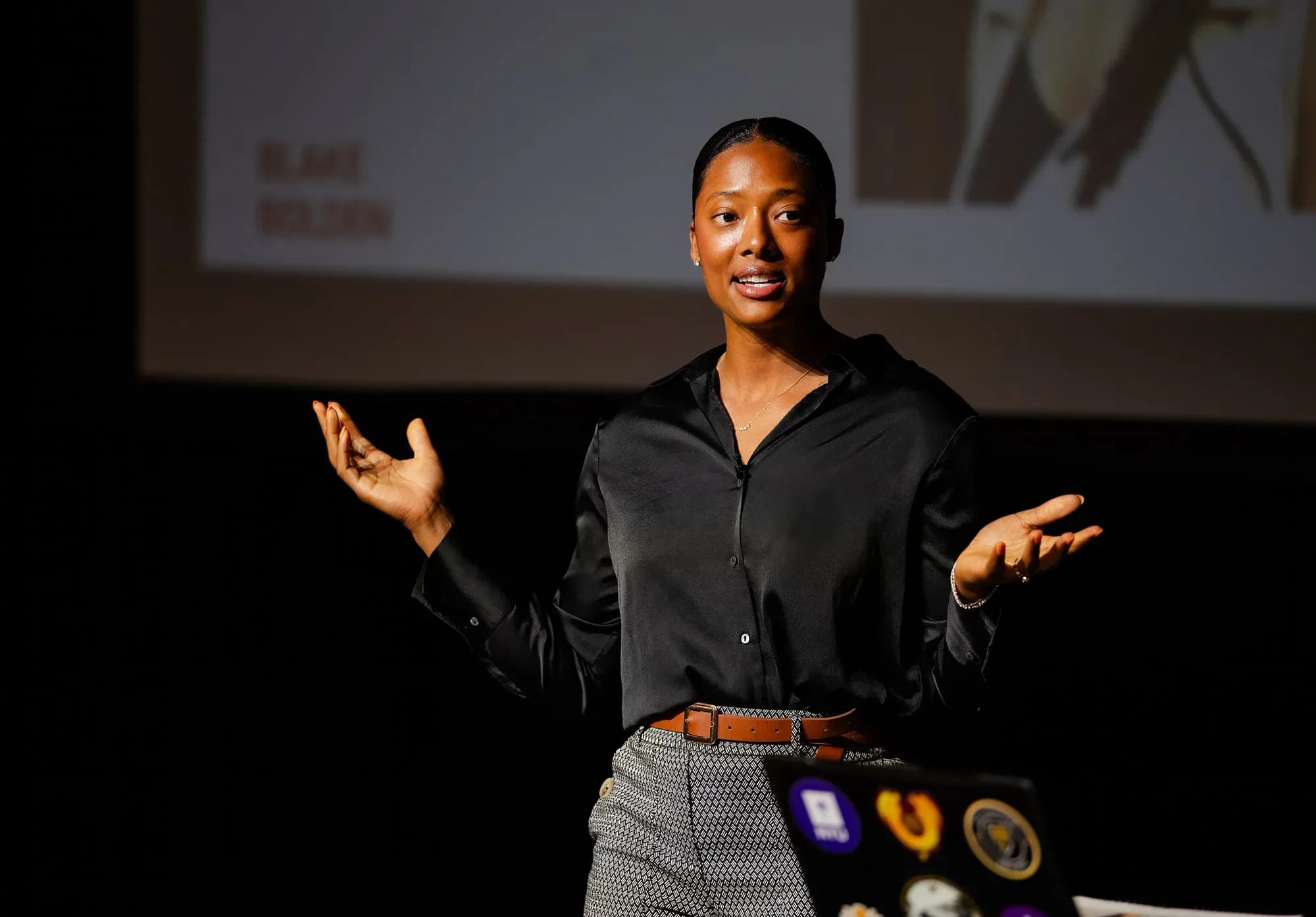 Blake Bolden on stage in a black silk shirt, hands open, mid-sentence