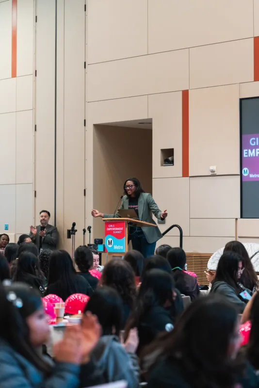 Blake Bolden at a Girls Empowerment Summit podium as a room of students applauds