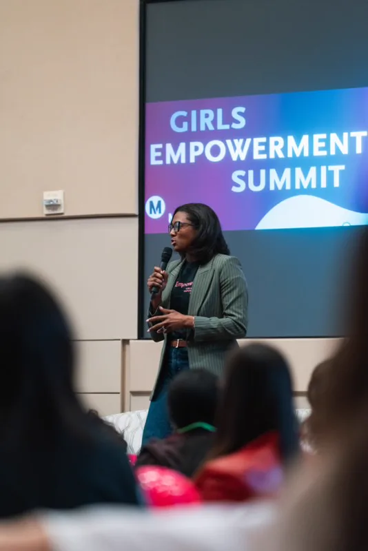 Blake Bolden speaking with a microphone in front of a Girls Empowerment Summit screen