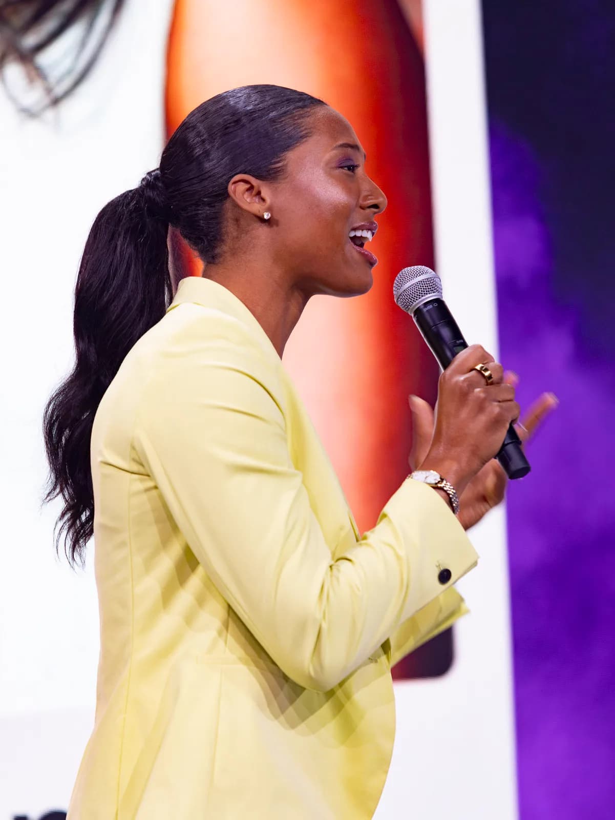 Blake Bolden on stage in a yellow blazer, speaking into a microphone